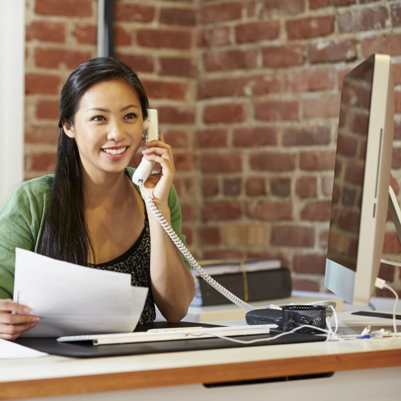Junge Frau arbeitet im modernen Büro am Computer und telefoniert mit Kunden.